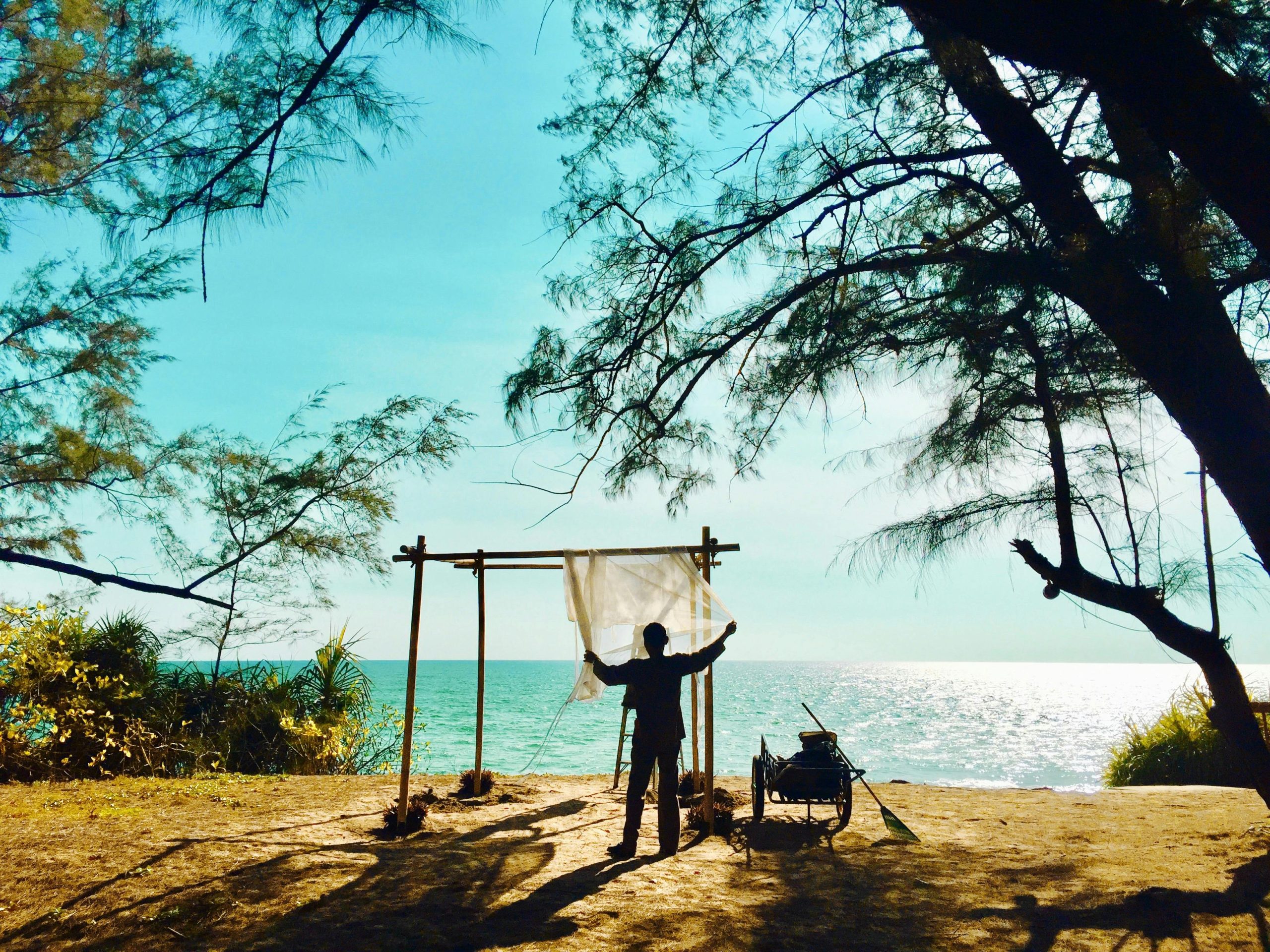 A silhouette of a person cleaning a net by the seashore at sunset, capturing a serene coastal landscape.