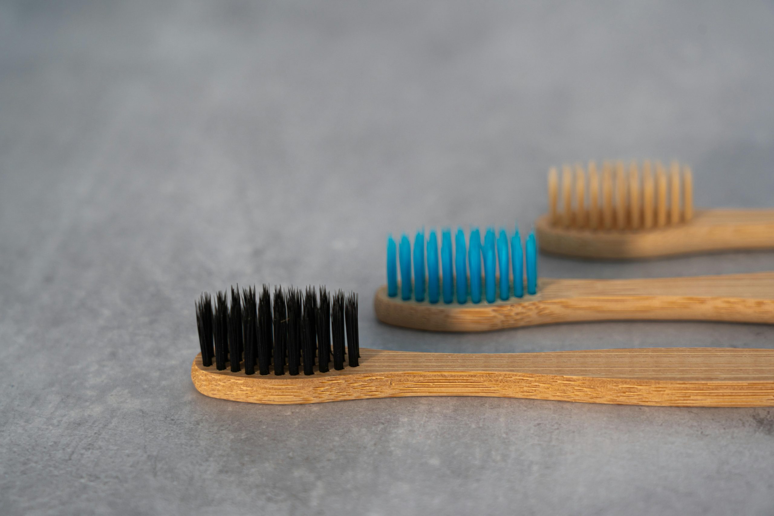 Close-up of three eco-friendly bamboo toothbrushes with colored bristles on a gray surface.