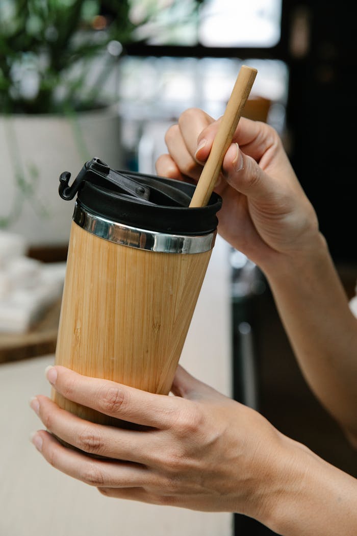 Hands holding eco-friendly bamboo tumbler with straw in a relaxed indoor setting.